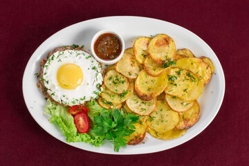 Delicious meat cutlet with egg with a side dish in the form of fried potatoes on a plate, menu for a restaurant