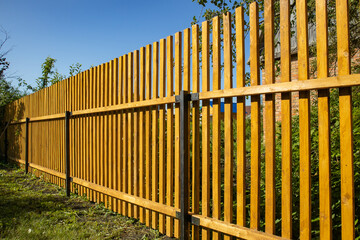 Close-up of a new wooden picket fence in the backyard of a country house, a sunny summer day
