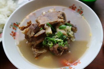 Sop Iga Sapi in white bowl on the wooden table. Beef Rib Soup is typical Indonesian dish, made from mixing beef ribs, carrots, leeks and celery. Selective focus.