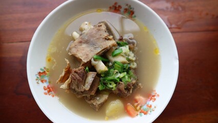 Sop Iga Sapi in white bowl on the wooden table. Beef Rib Soup is typical Indonesian dish, made from mixing beef ribs, carrots, leeks and celery. Selective focus.