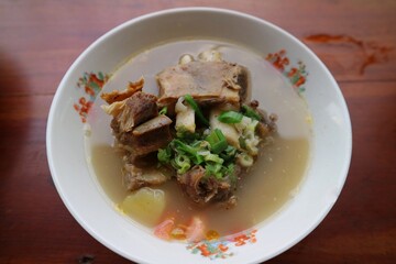Sop Iga Sapi in white bowl on the wooden table. Beef Rib Soup is typical Indonesian dish, made from mixing beef ribs, carrots, leeks and celery. Selective focus.