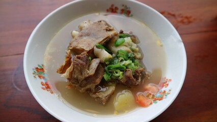 Sop Iga Sapi in white bowl on the wooden table. Beef Rib Soup is typical Indonesian dish, made from mixing beef ribs, carrots, leeks and celery. Selective focus.