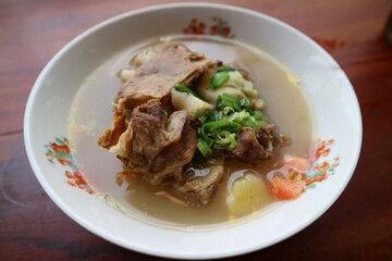 Sop Iga Sapi in white bowl on the wooden table. Beef Rib Soup is typical Indonesian dish, made from mixing beef ribs, carrots, leeks and celery. Selective focus.