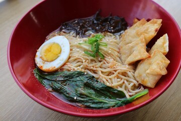 Gyoza dumplings and Ramen in the re bowl on the wooden table. Served with boiled egg, vegetable and mushroom.