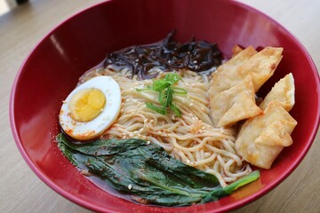 Gyoza dumplings and Ramen in the re bowl on the wooden table. Served with boiled egg, vegetable and...