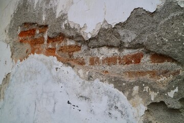 texture of a wall with destroyed bricks, crumbling plaster and damaged protective paint, abstract background. Brick wall with crumbling plaster.