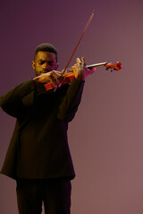Man in black suit playing violin on purple background in elegant and enchanting musical performance...