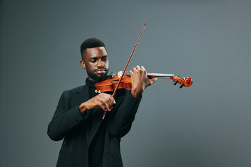 Talented African American man in elegant suit playing violin on gray background in studio portrait
