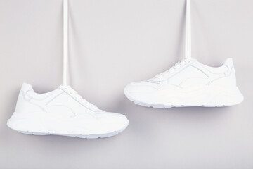 Pair of hanging white shoes on grey background