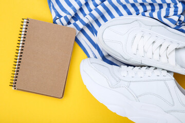 Pair of white shoes with striped t-shirt and notepad on yellow background - 760324432