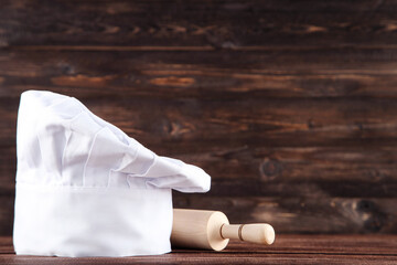 Chef hat with rolling pin on wooden background