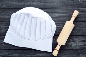 Chef hat with rolling pin on black wooden background