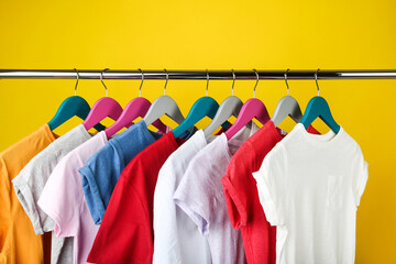 Wooden hangers with clothes on yellow background