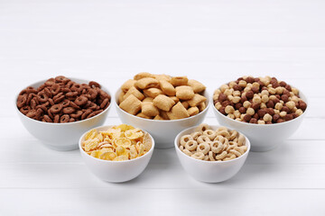 Various corn flakes in bowls on white wooden table
