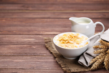 Corn flakes in bowl with milk and jar on brown wooden table - 760324890