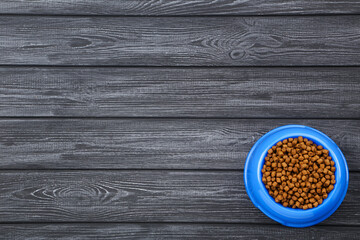 Dry pet food in bowl on black wooden table