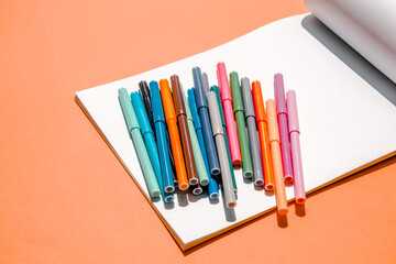 Colorful markers and sheets of an album on orange background.