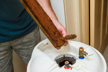 Person holds in his hand a damaged electric heating element from boiler. - 760333070