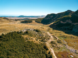 Drone shot of a glacial lake with peaks, meadows and scattered trees, during autumn, Durmitor, Montenegro
