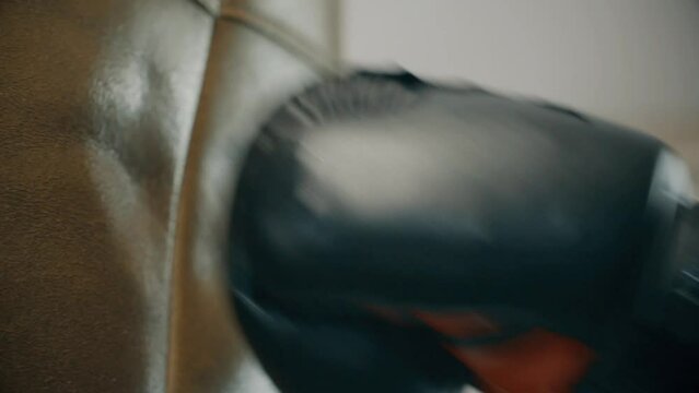 Close-up of a man's hands wearing a boxing glove hitting a punching bag
