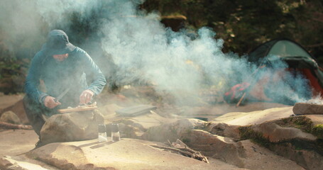 A man cooks food outdoors on a camping trip while sitting by a campfire. Cooking food on a tourist...