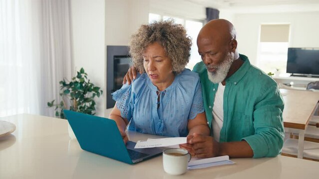 Mature couple with laptop at home worried about debt how to pay bills and rising cost of living - shot in slow motion