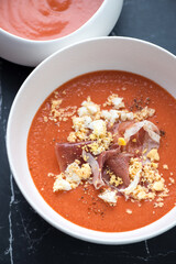 Spanish traditional salmorejo served with prosciutto and grated egg in a white bowl, vertical shot, middle close-up