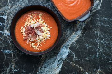 Bowl with spanish salmorejo or cold tomato and bread soup, top view on a black marble background,...