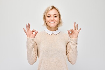 Smiling woman making okay gesture, isolated on light background.