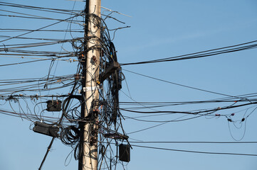 Electric post and line are on blue background.Electric post is covered by busy electric line.