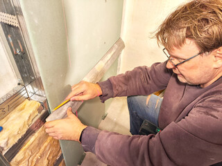Professional Installs Drywall During Home Renovation. A skilled worker measures and secures drywall in home under renovation
