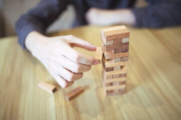Business strategy concept with hands playing a wooden block tower game, symbolizing risk and stability. Planning risk management