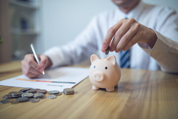 Person in a business shirt saving money in a piggy bank, with coins and financial reports on the...