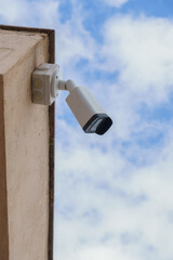 surveillance camera on a wall with a cloudy sky in the background