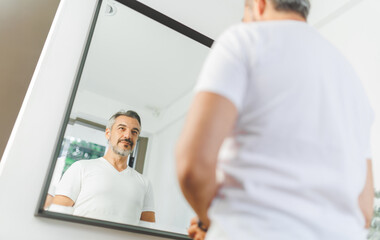 Naklejka na ściany i meble Confident mature man in white T-shirt admiring his reflection, showcasing self-assurance and personal care