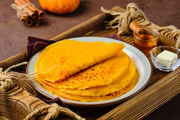 Thin pumpkin pancakes in a stack on a gray ceramic plate on a brown concrete background. Pancake recipes. International Pancake Day.