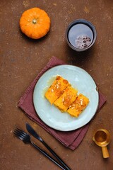 Thin pumpkin pancakes rolled into a roll and topped with honey and jam on a gray ceramic plate on a brown concrete background. Pancake recipes.