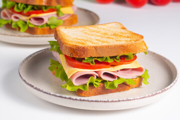 Close-up of two sandwiches with bacon, salami, prosciutto and fresh vegetables on rustic wooden cutting board. Club sandwich concept - 760433040