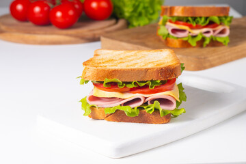 Close-up of two sandwiches with bacon, salami, prosciutto and fresh vegetables on rustic wooden cutting board. Club sandwich concept - 760433079