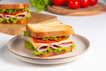 Close-up of two sandwiches with bacon, salami, prosciutto and fresh vegetables on rustic wooden cutting board. Club sandwich concept - 760433096