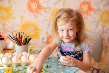 a little girl with red hair paints Easter eggs. genuine sincere emotions of joy, surprise and excitement. Preparing for Easter in the family circle.
