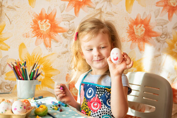 a little girl with red hair paints Easter eggs. genuine sincere emotions of joy, surprise and excitement. Preparing for Easter in the family circle.