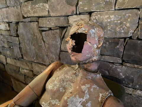 Portrait of wooden vintage scary dummy doll on the background of stone wall with a hole on its face