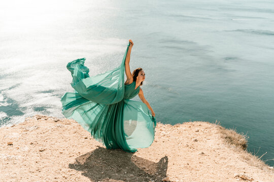 Woman green dress sea. Female dancer posing on a rocky outcrop high above the sea. Girl on the nature on blue sky background. Fashion photo.