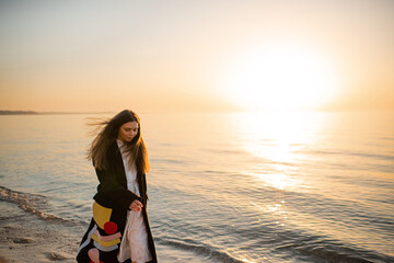 Stylish young woman wearing trendy jacket and dress walking at sea coast line over sunset outdoor....