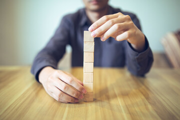 Hand strategically placing wooden blocks in a stair-step design on a table, signifying progressive...