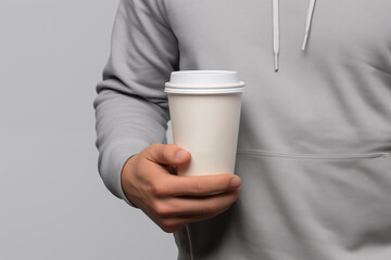 Mockup of a man hand holding a paper cup of coffee isolated on a light gray background