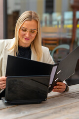 a business woman sits in front of a cafe and reads a file folder