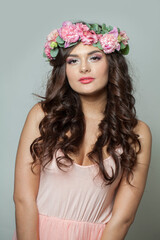 Charming female model in floral summer wreath on her hair. Young woman with clean skin and wavy hairstyle on white background