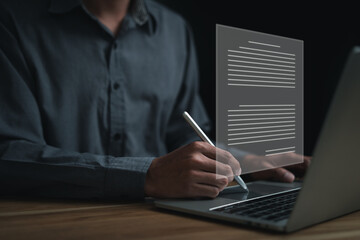 A man is writing on a laptop with a pen